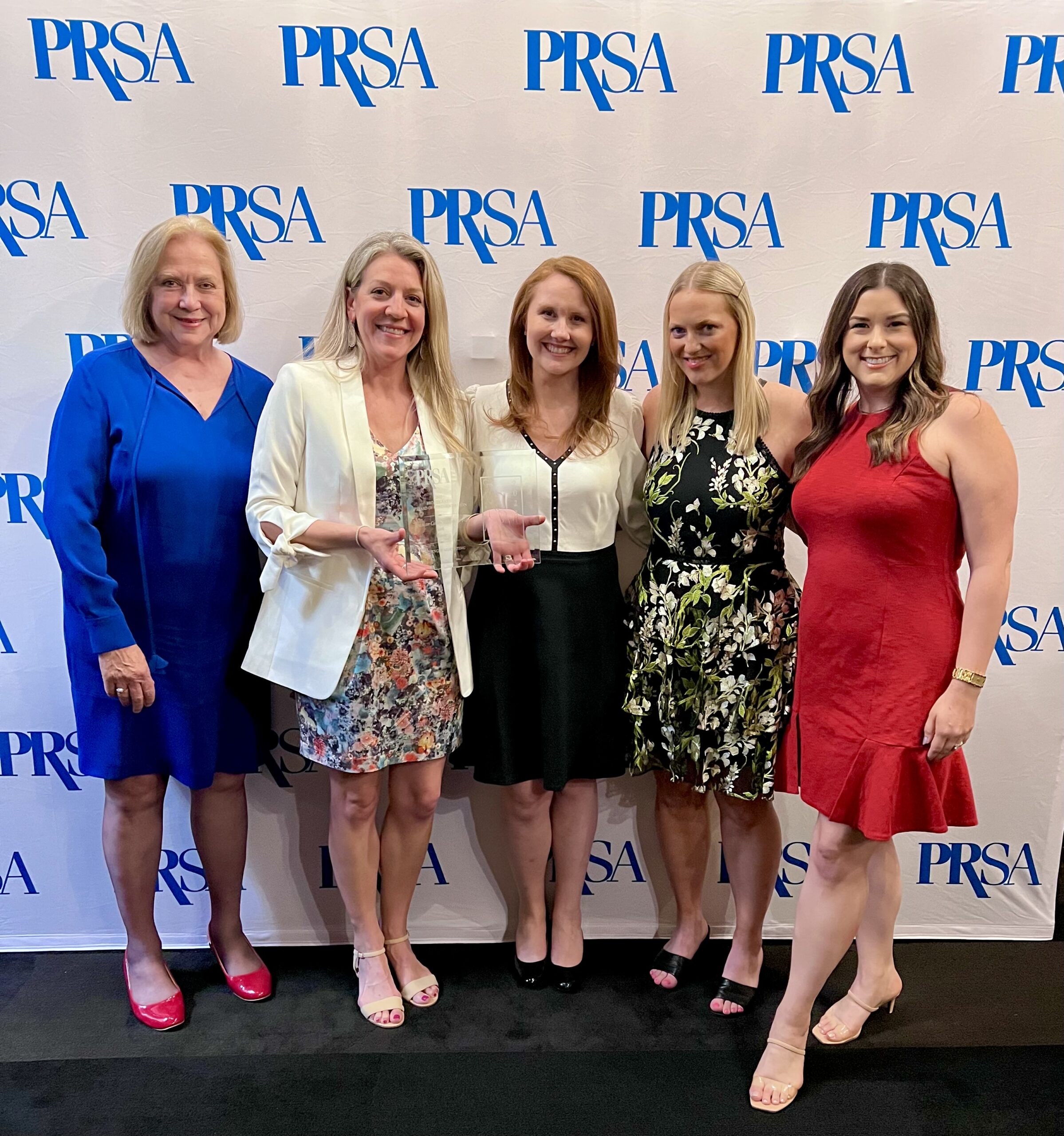 Five women standing in front of a PRSA-brand banner holding an award.